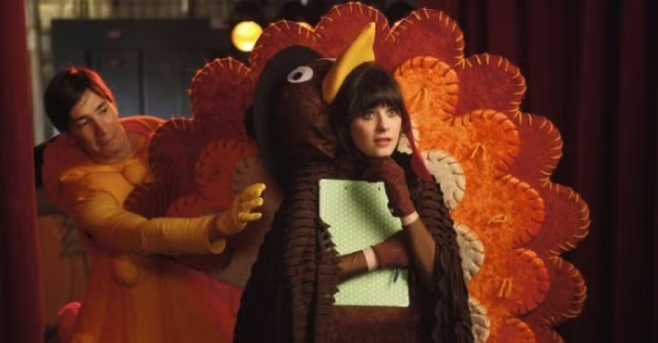 Jess from New Girl in a turkey costume with a guy behind her also in costume. 